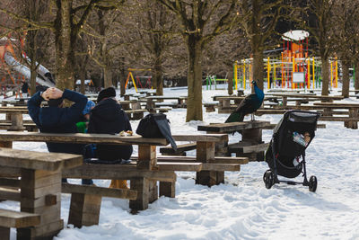 People sitting on snow covered plants during winter