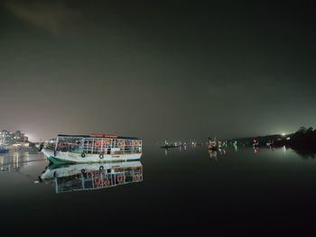 Illuminated buildings by sea against sky at night