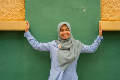 Portrait of smiling young woman standing against wall