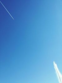 Low angle view of vapor trails against clear blue sky