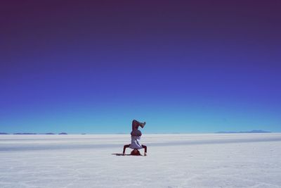 Woman doing handstand on salt flat against clear blue sky