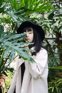 Woman wearing hat standing against plants