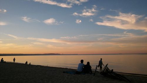 Silhouette people sitting on beach against sky during sunset