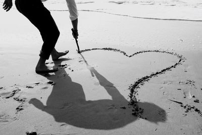 Low section of person making heart shape at sandy beach