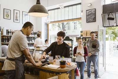 Male customer paying at checkout counter while doing shopping in deli