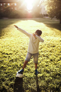 Full length of boy with soccer ball covering face while standing on grassy field at park