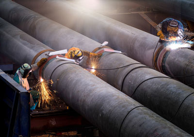 Three workers welding on pipeline in factory