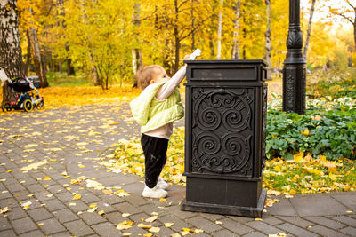 Cute little baby throws trash into trash can in autumn park. instilling cultural norms from birth