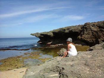 Man sitting on rock by sea against sky