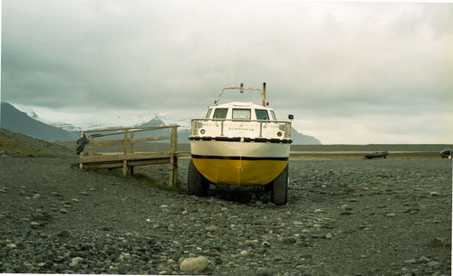 Boat moored at beach against cloudy sky