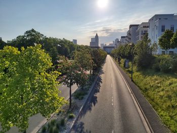Road by trees in city against sky
