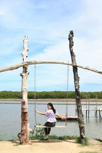 Full length of woman on swing in playground against sky