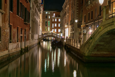 Bridge over canal amidst buildings in venice at night