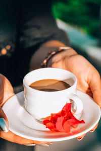 Tanned woman holding porcelain cup of hot coffee and pink tropical flower. mug of hot coffee 