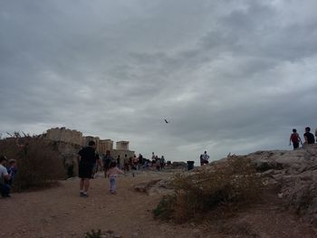 People standing on landscape against cloudy sky