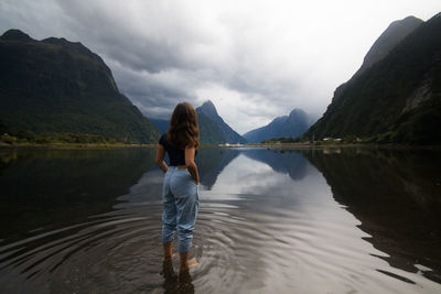 Rear view of woman standing in lake against mountains and sky