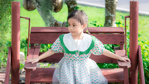 Cute baby asian girl, little preschooler child sitting on swing chair and looking to the left.