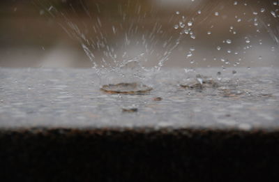 Close-up of water splashing on glass table against black background