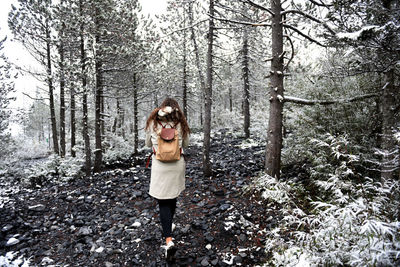 Young woman standing by tree trunk in forest