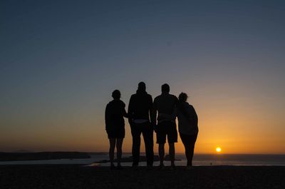 Silhouette people on beach against clear sky during sunset