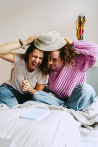 Playful female friends wearing hat while spending leisure time together at home