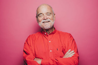 Smiling senior man with eyes closed against pink background