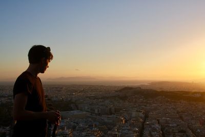 Man looking at cityscape against sky during sunset