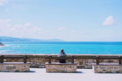 Man sitting by sea against sky