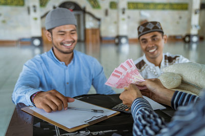 Smiling men receiving cash from person at mosque