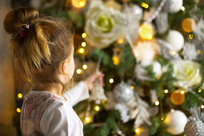 Rear view of girl holding christmas tree decoration at home
