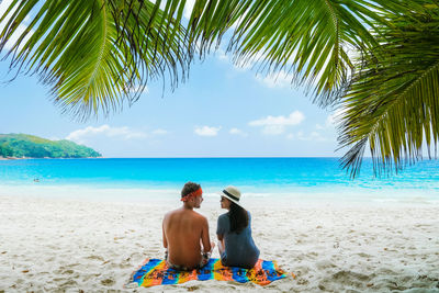 Rear view of woman sitting on beach against sky