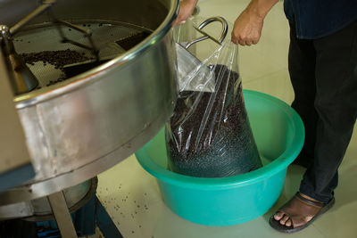 Low section of manual worker collecting roasted coffee beans from machinery in factory