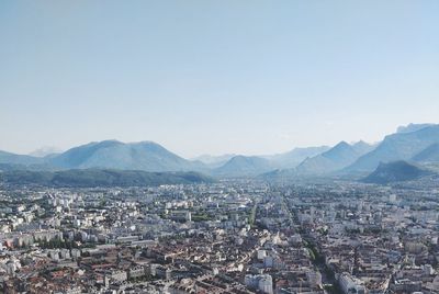 Aerial view of city by mountains against clear sky