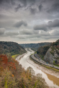 Scenic view of river by tree mountains against cloudy sky