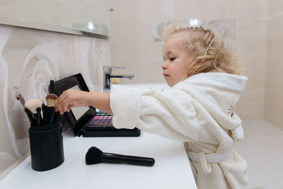 Toddler girl doing herself makeup with mama's cosmetics pretending grownup. applying eyeshadows