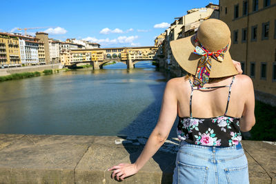 Rear view of woman standing by river against buildings