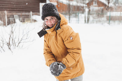 Girl in plays in backyard and enjoys sunny day in winter, she stands on snowdrift 