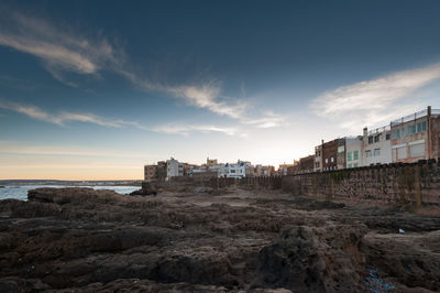 Buildings by sea against sky during sunset