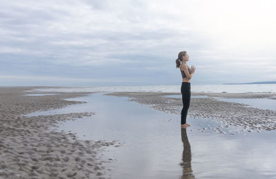 Woman meditating at the coast at low tide, soft light. getting away from it all.