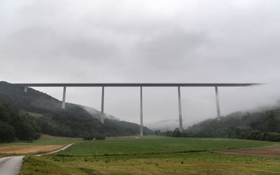 Bridge over field against sky during foggy weather