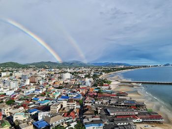 High angle view of rainbow over sea and buildings in city