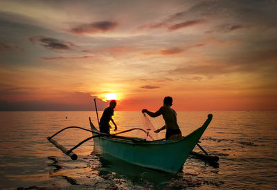 Silhouette people in sea against sky during sunset