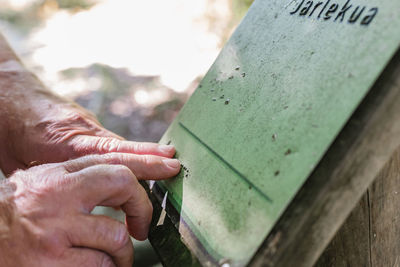 Cropped anonymous blind elderly traveler touching and reading braille on signboard while visiting park on summer weekend day