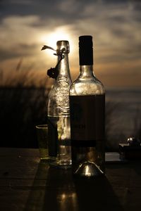 Close-up of beer bottle against sea during sunset