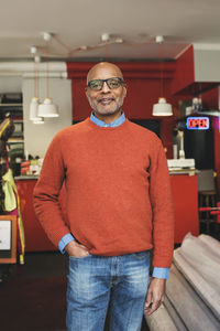 Portrait of smiling confident owner standing with hand in pocket at store