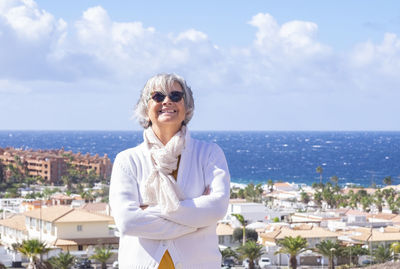 Portrait of smiling senior woman standing against sea in city