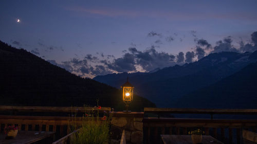 Illuminated building by mountains against sky at night