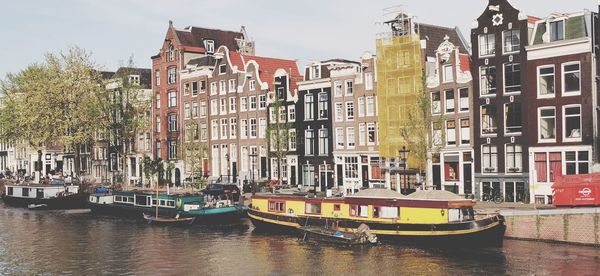 Boats in river by buildings in city against sky