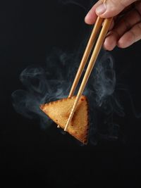 Close-up of hand holding burning candle against black background