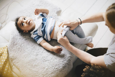 Mother with boy dressing toddler by sofa at home